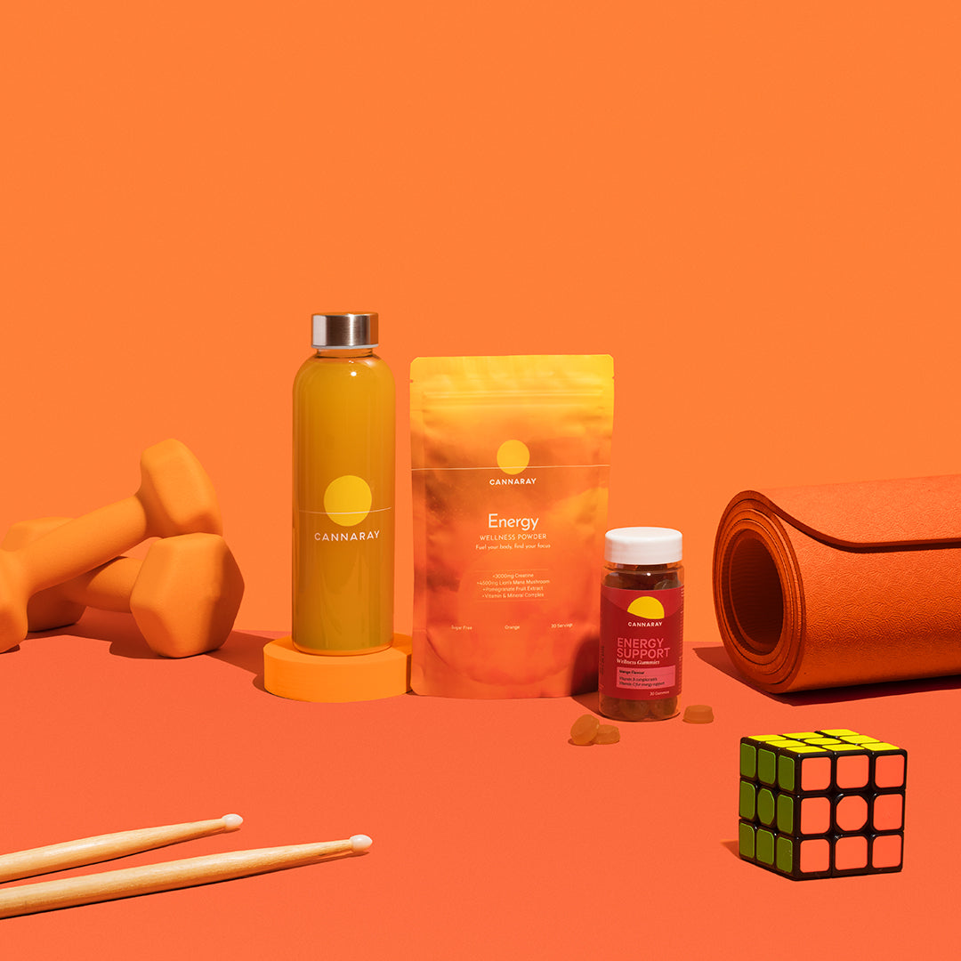 Cannaray water bottle, Energy Powder and Energy Support Gummies surrounded by weight and a yoga mat against an orange background.