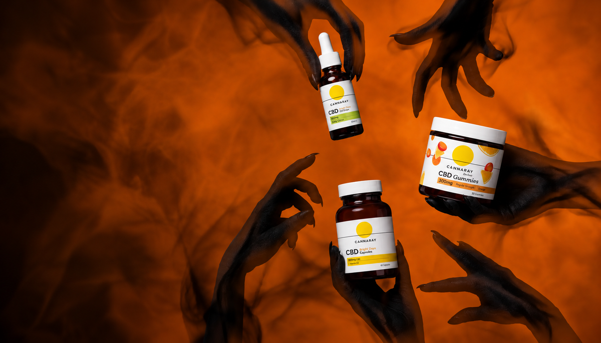 Cannaray Bright Days CBD oil, gummies and capsules held by Halloween hands on an orange smoky background